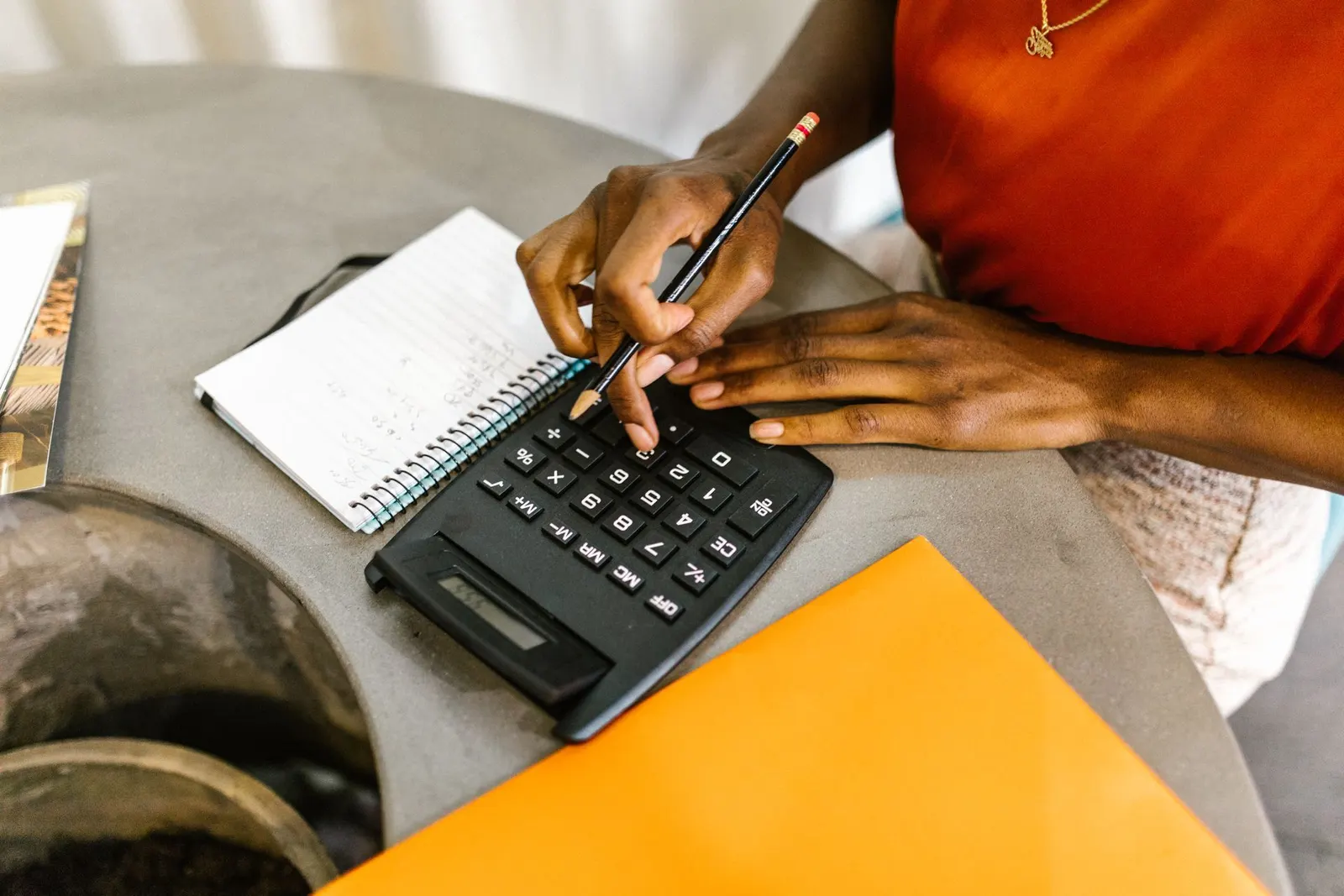 Hands working out figures with a calculator, a pen and a notebook.